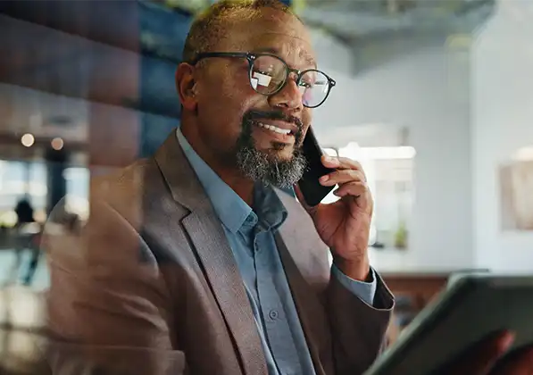 A man in a gray business suit talking on his smart phone while looking at a tablet